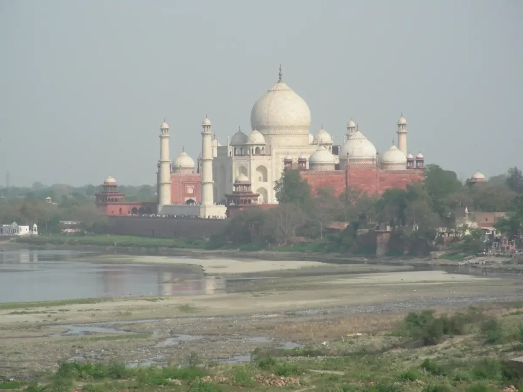 What are the must-visit attractions in Agra? 1 The white marble Taj Mahal with its minarets and domes, seen from across the Yamuna River, surrounded by greenery and red sandstone structures.