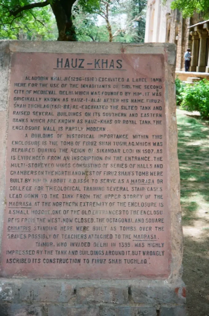 Hauz Khas 1 Stone plaque at the entrance of the Hauz Khas complex in Delhi, describing the historical significance of the site, including the excavation by Alauddin Khalji, restoration by Firuz Shah Tughlaq, and details about the madrasa, tombs, and surrounding structures.