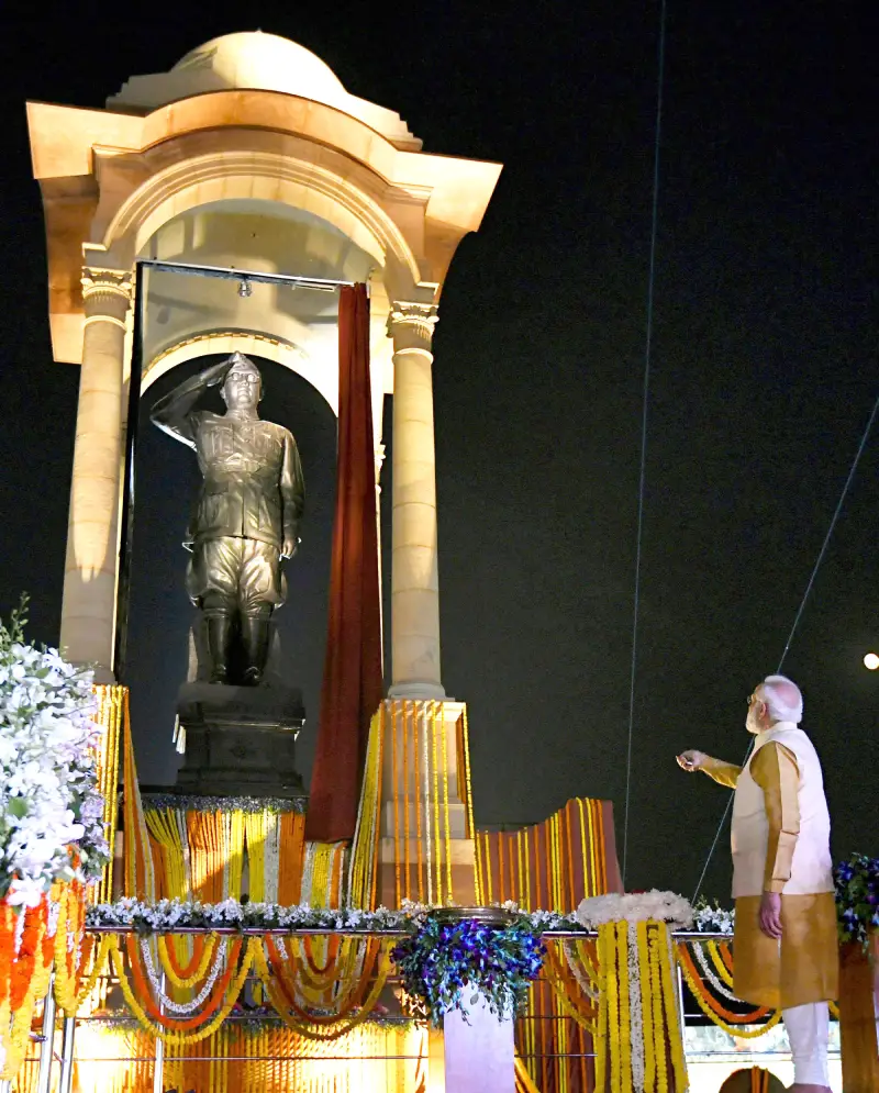 Prime Minister Narendra Modi unveils a statue of Netaji Subhas Chandra Bose at India Gate, New Delhi, during the inauguration of the ‘Kartavya Path’ on September 8, 2022. The statue, housed under a grand stone canopy and illuminated at night, shows Bose in a military uniform saluting. The stage is decorated with colorful flower garlands and lights, creating a ceremonial atmosphere.