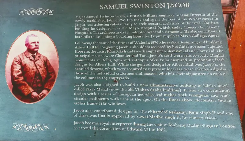 Albert Hall Museum 2 Informational display panel about Samuel Swinton Jacob, a British military engineer and architect, featuring a sepia-toned portrait of him on the left. The text describes Jacob’s contributions to Jaipur's architecture after he became Director of the Jaipur PWD in 1867. It highlights his role in designing the Mayo Hospital, boarding houses, Albert Hall, and other Indo-Saracenic style buildings. The panel also notes his collaboration with local craftsmen and his influence on major architectural projects in Delhi, Agra, and Fatehpur Sikri. His involvement in designing the Jaleb Chowk's Naya Mahal and serving as a royal interpreter during King Edward VII’s coronation in 1902 is also mentioned.